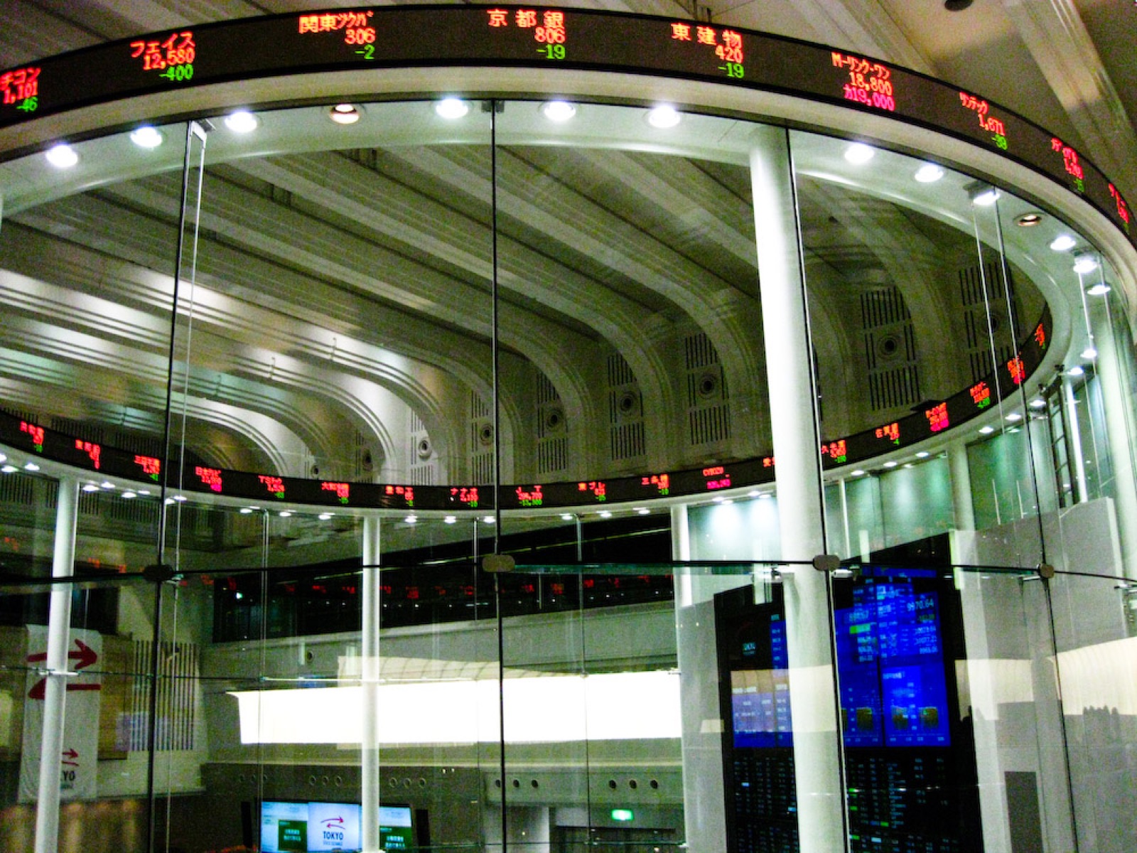 A curved exchange ticker board glowing with green and orange share prices.